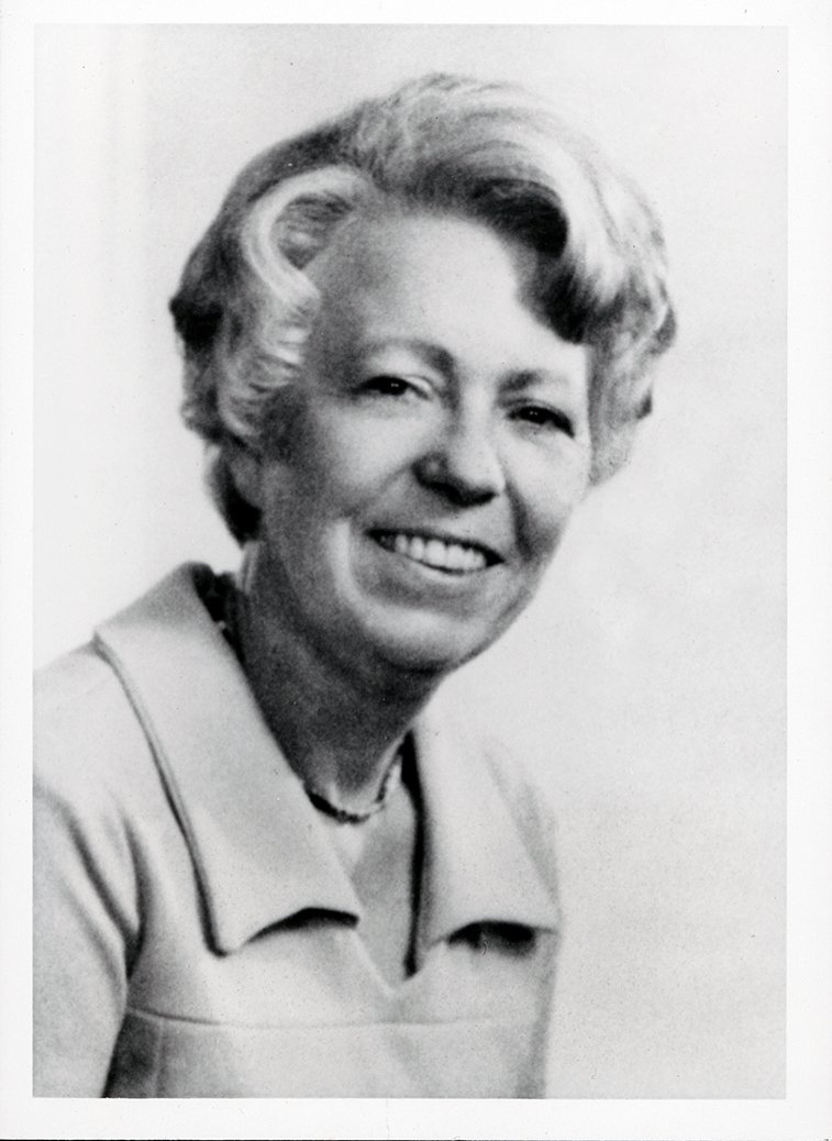 Image Description. Black and white photograph of a Caucasian woman with short, curled gray hair, smiling.