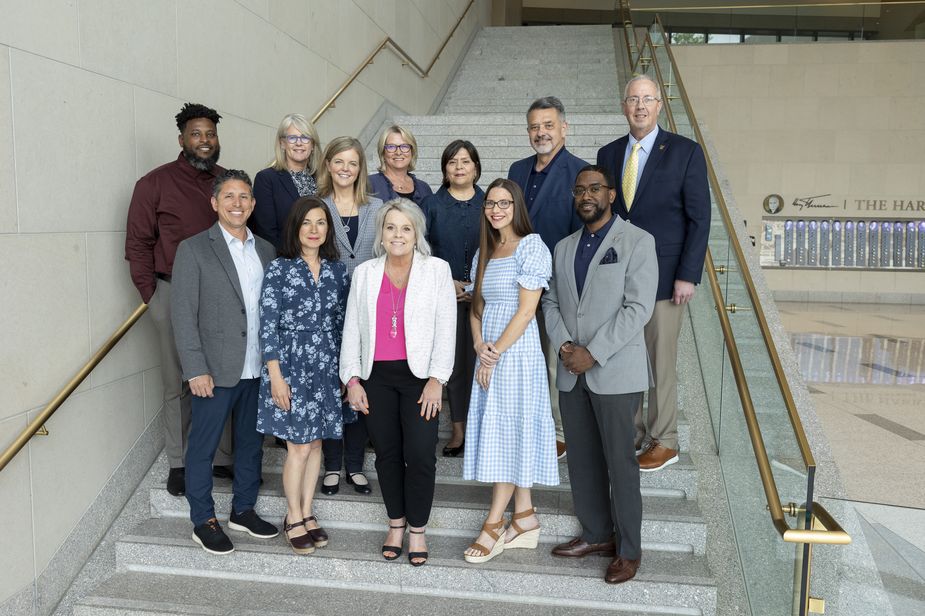 Members of the CDAC gather in two rows on the tall set of stairs in the Kansas City Fed lobby. The front row include five people - two men and three women. The back row includes four women and three men. It's a mix of races and ethnicities, and ages. Some are in suits, others are dressed more casually. All are smiling.