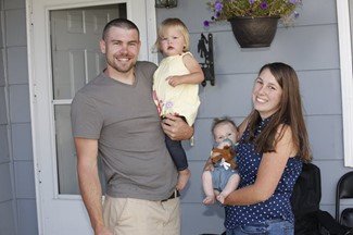 Photo of mom, dad and two young children on the porch of their house.