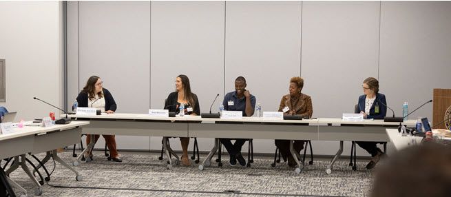 The photo shows the moderator and four panelists assembled to talk about affordable housing. All are smiling. The moderator is a white woman, the first panelist is a white woman, the second is a black man, the third is a black woman, and the fourth is a white woman. All are in suits.