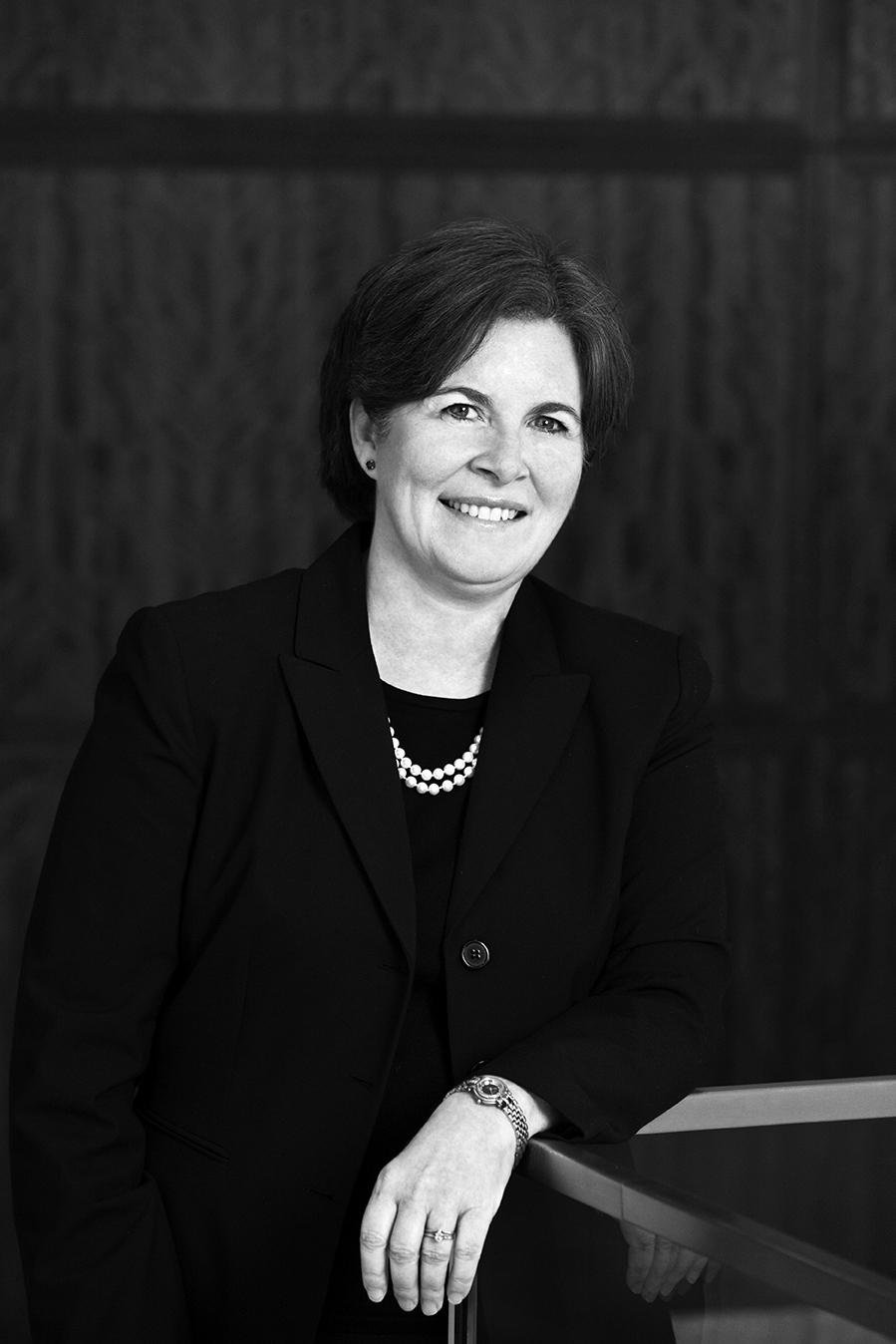 Image Description. Black and white photograph of a Caucasian woman with short brown hair standing in an office, smiling.